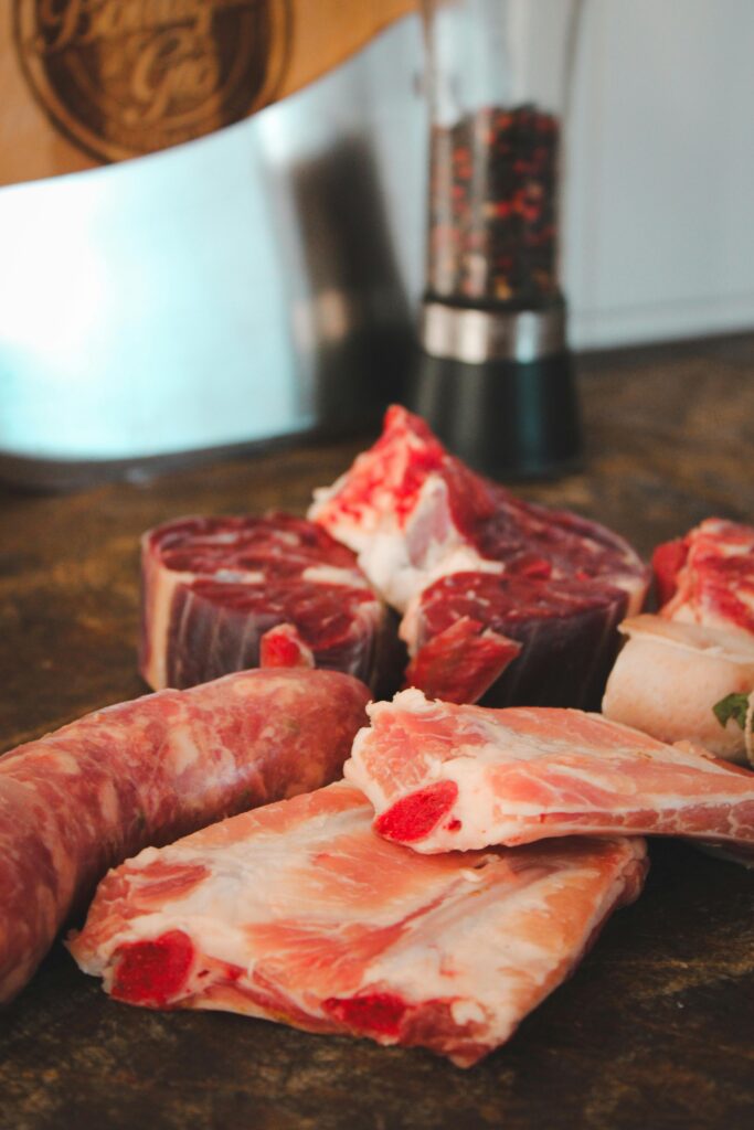 Various cuts of raw meat on a rustic kitchen table with a pepper grinder in the background.