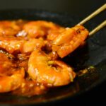 Close-up of spicy prawns in sauce with chopsticks on a dark plate
